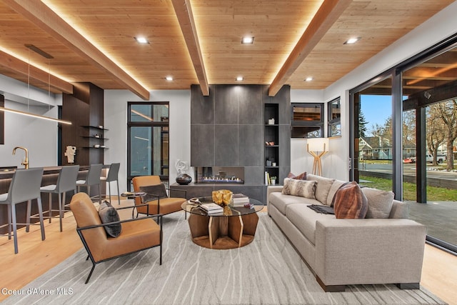 living room featuring sink, light hardwood / wood-style flooring, beam ceiling, a fireplace, and wooden ceiling