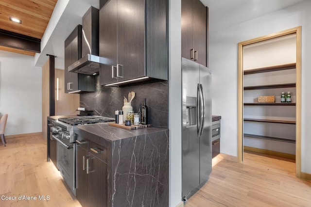 kitchen with dark brown cabinetry, appliances with stainless steel finishes, decorative backsplash, and wall chimney range hood