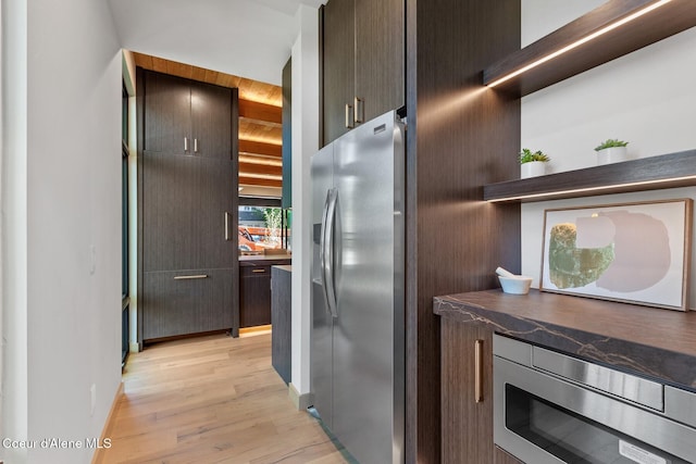 kitchen with dark stone countertops, dark brown cabinetry, stainless steel appliances, and light wood-type flooring