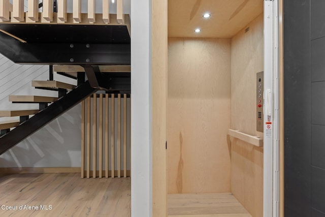 stairway with elevator and hardwood / wood-style floors