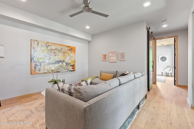 living room featuring ceiling fan, a barn door, and light hardwood / wood-style floors