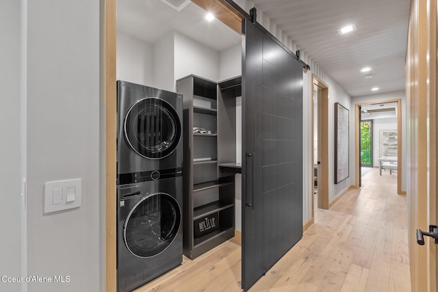 washroom with stacked washer and dryer, light hardwood / wood-style floors, and a barn door