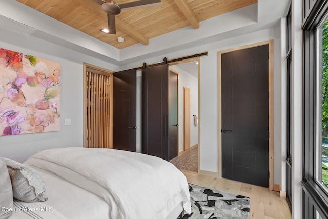 bedroom with beamed ceiling, a barn door, wood ceiling, and light hardwood / wood-style flooring