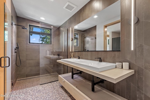 bathroom with tile walls, a shower with shower door, and double sink