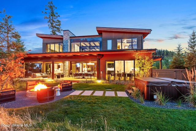 2763 E Lower Pasture Rd, Harrison, ID 83833 - back house at dusk with a hot tub, an outdoor living space with a fire pit, a lawn, and a patio area