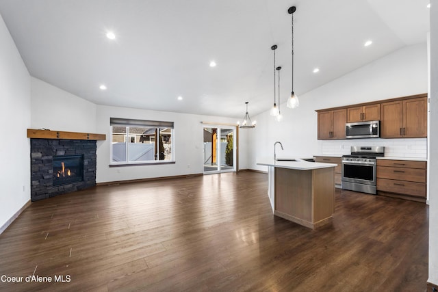 kitchen featuring a stone fireplace, sink, hanging light fixtures, appliances with stainless steel finishes, and an island with sink