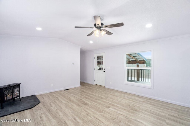 unfurnished living room with vaulted ceiling, a wood stove, ceiling fan, crown molding, and light hardwood / wood-style flooring