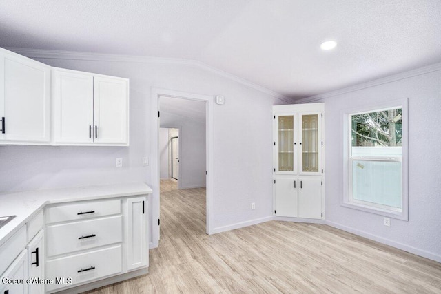 kitchen with lofted ceiling, crown molding, white cabinets, and light wood-type flooring