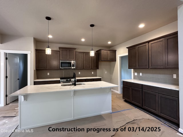 kitchen with stainless steel microwave, dark brown cabinets, decorative backsplash, and a sink