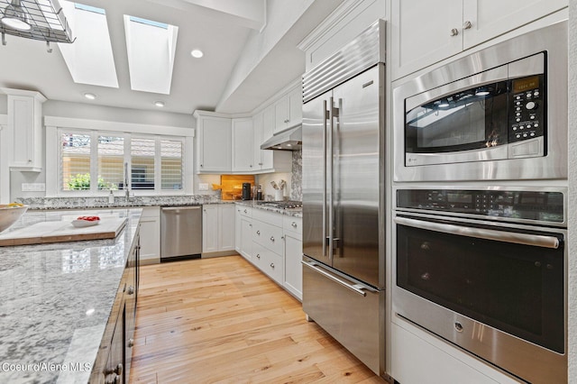 kitchen featuring built in appliances, light stone countertops, white cabinets, and light wood-type flooring