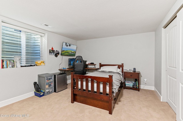 carpeted bedroom featuring a closet, stainless steel fridge, and a textured ceiling