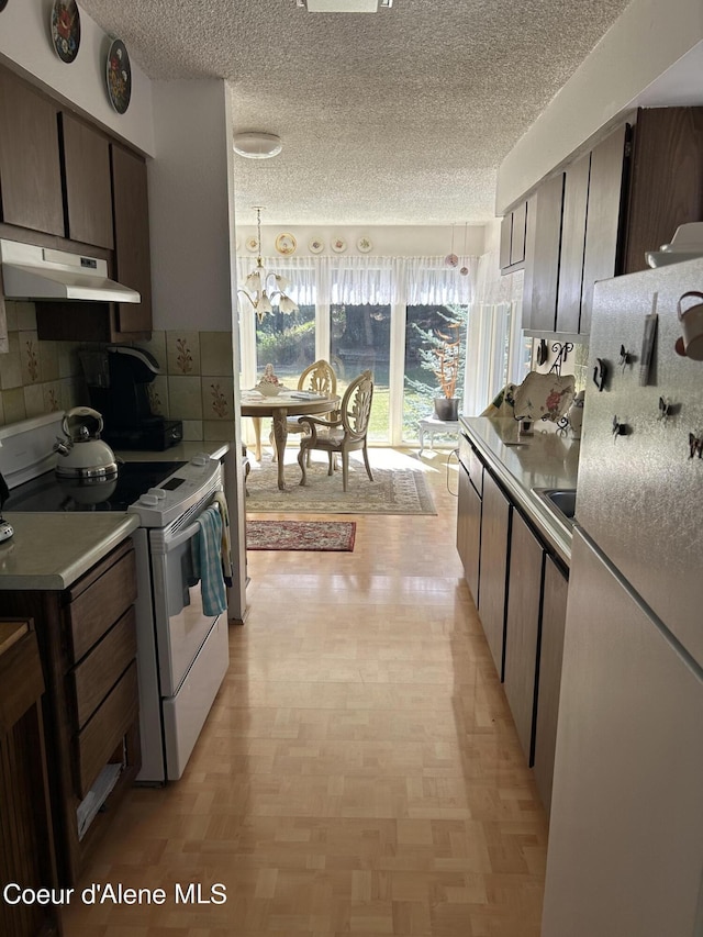 kitchen featuring a textured ceiling, a notable chandelier, pendant lighting, white appliances, and backsplash