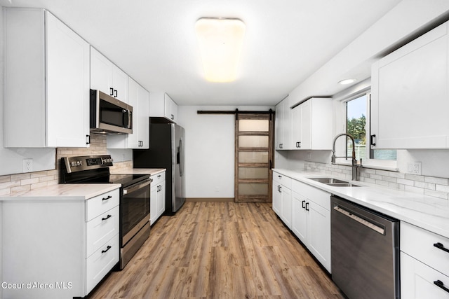 kitchen featuring sink, appliances with stainless steel finishes, backsplash, white cabinets, and a barn door