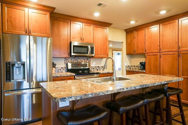 kitchen with sink, a center island with sink, appliances with stainless steel finishes, a kitchen breakfast bar, and light stone countertops