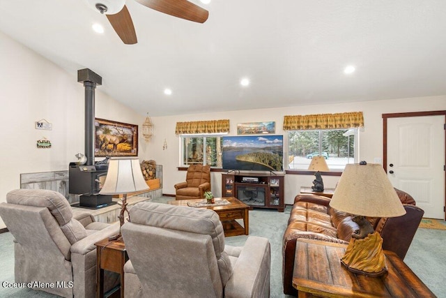 carpeted living room featuring lofted ceiling, ceiling fan, and a wood stove