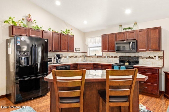 kitchen with decorative backsplash, vaulted ceiling, black appliances, and a kitchen breakfast bar