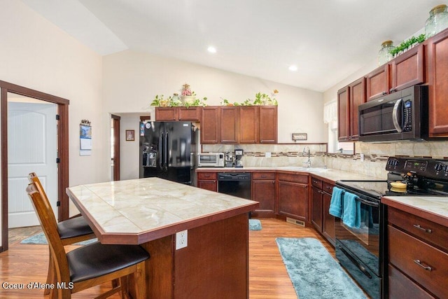 kitchen with sink, a center island, black appliances, a kitchen bar, and vaulted ceiling