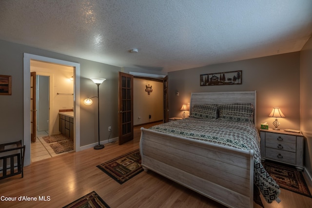 bedroom with ensuite bathroom, a textured ceiling, and light wood-type flooring