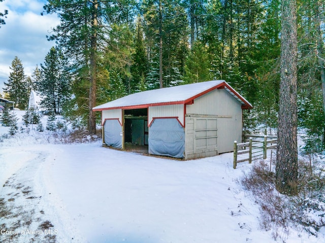 snow covered garage featuring a garage and fence