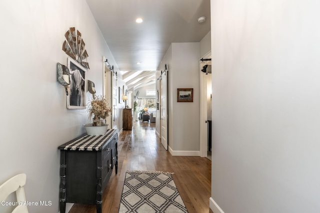 hall featuring lofted ceiling, a barn door, wood finished floors, and baseboards