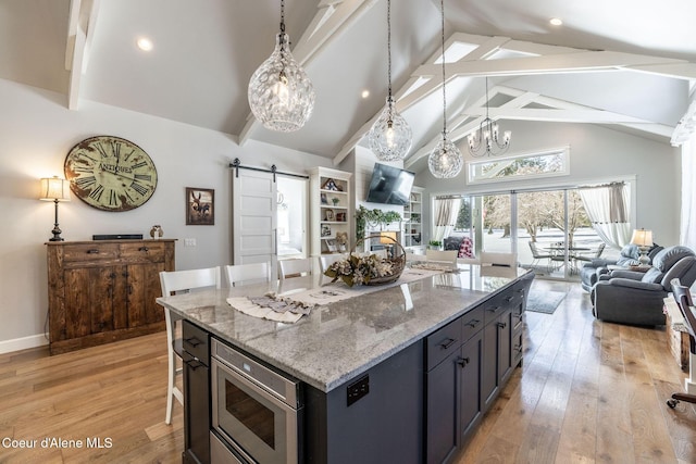 kitchen featuring a barn door, open floor plan, light wood-type flooring, beam ceiling, and stainless steel microwave