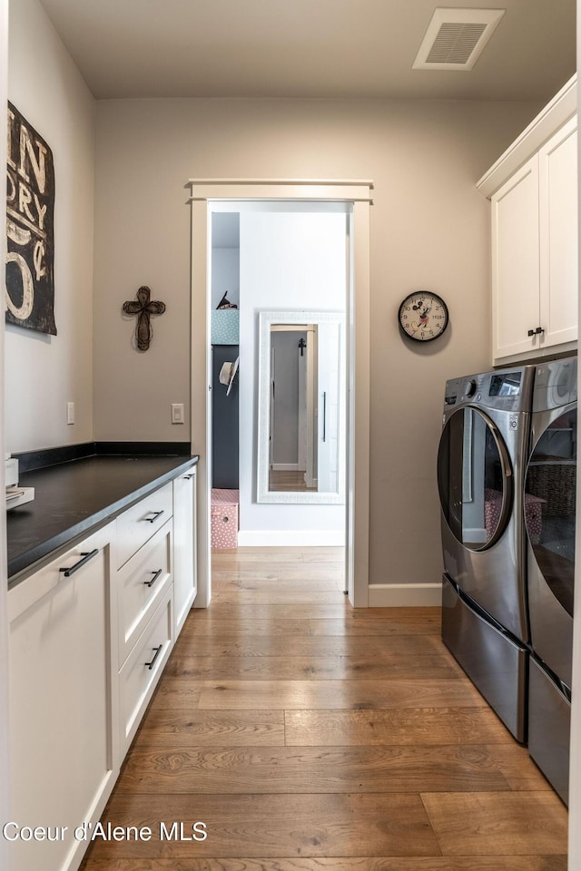 washroom featuring wood finished floors, visible vents, baseboards, cabinet space, and washer and clothes dryer