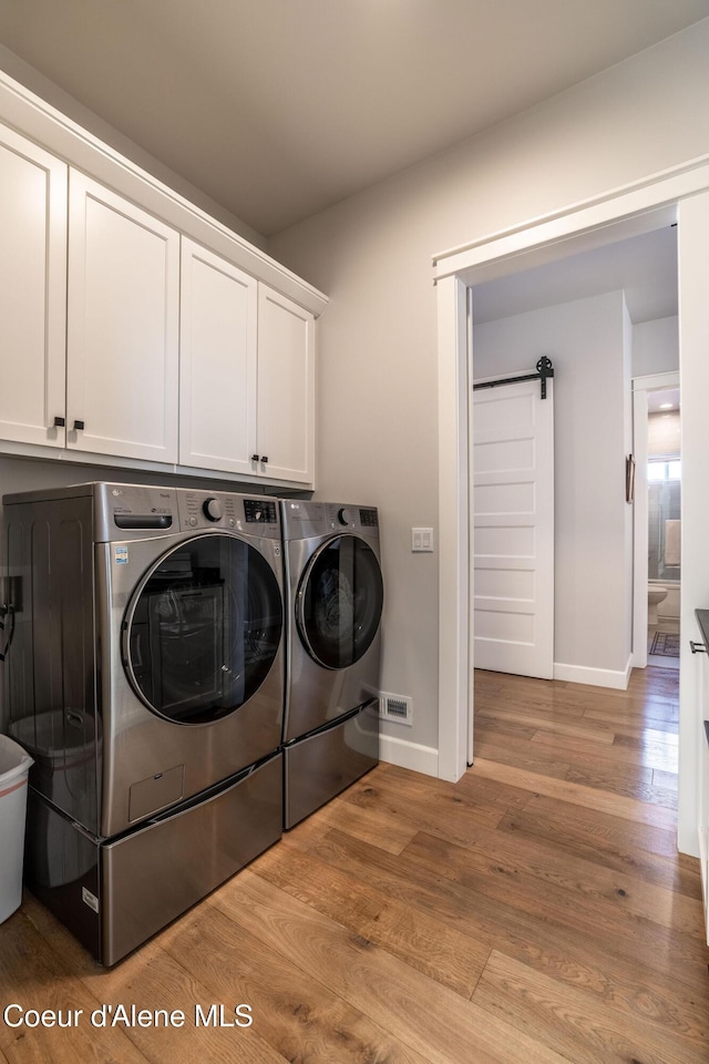 clothes washing area featuring a barn door, baseboards, cabinet space, light wood finished floors, and washing machine and clothes dryer