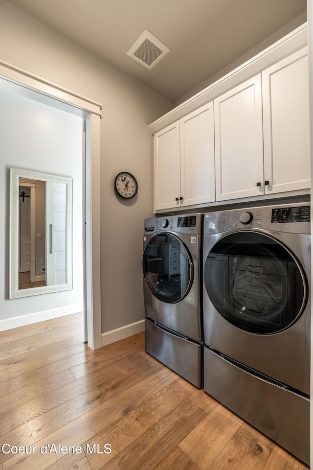 washroom featuring cabinet space, visible vents, washing machine and dryer, light wood-type flooring, and baseboards