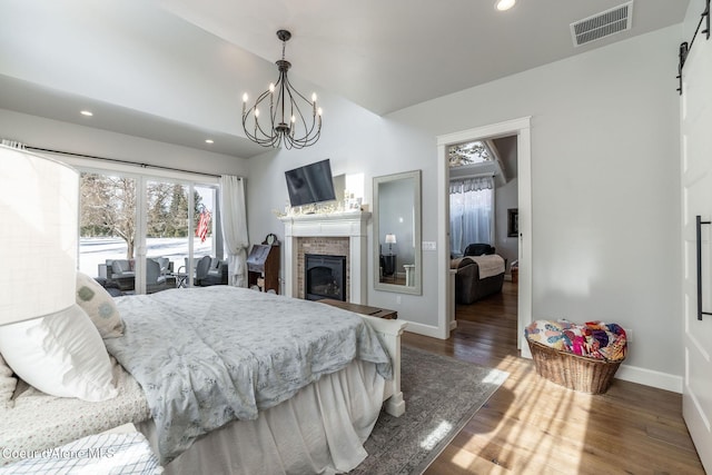 bedroom with a barn door, recessed lighting, a fireplace, wood finished floors, and visible vents