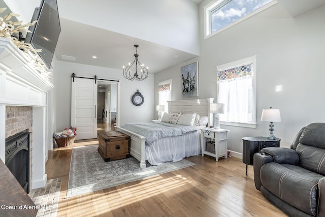 bedroom with a barn door, a brick fireplace, baseboards, light wood-style floors, and a notable chandelier