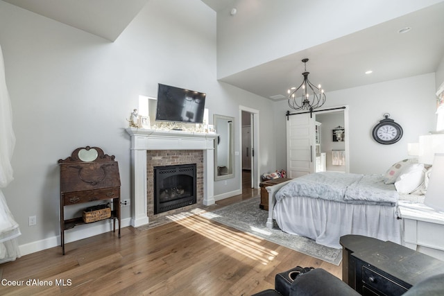 bedroom with a barn door, a notable chandelier, a fireplace, wood finished floors, and baseboards