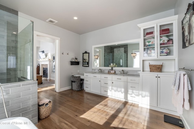 full bathroom featuring double vanity, visible vents, a glass covered fireplace, wood finished floors, and a shower stall