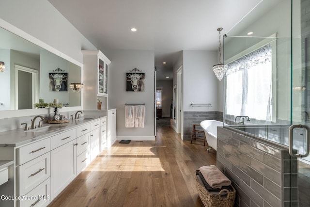 full bath featuring double vanity, a sink, wood finished floors, a chandelier, and a freestanding tub