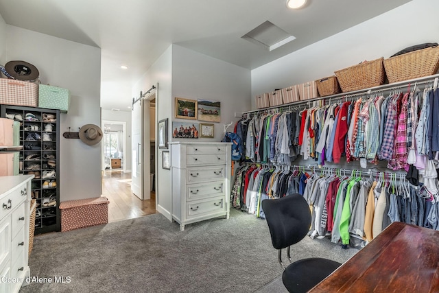 walk in closet with a barn door, carpet, and attic access