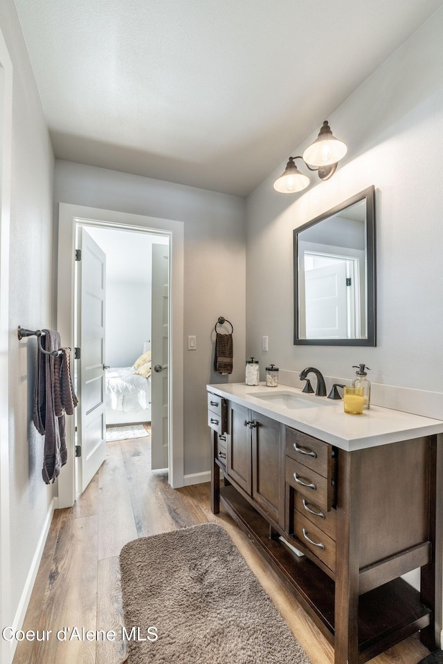 bathroom with ensuite bath, baseboards, wood finished floors, and vanity