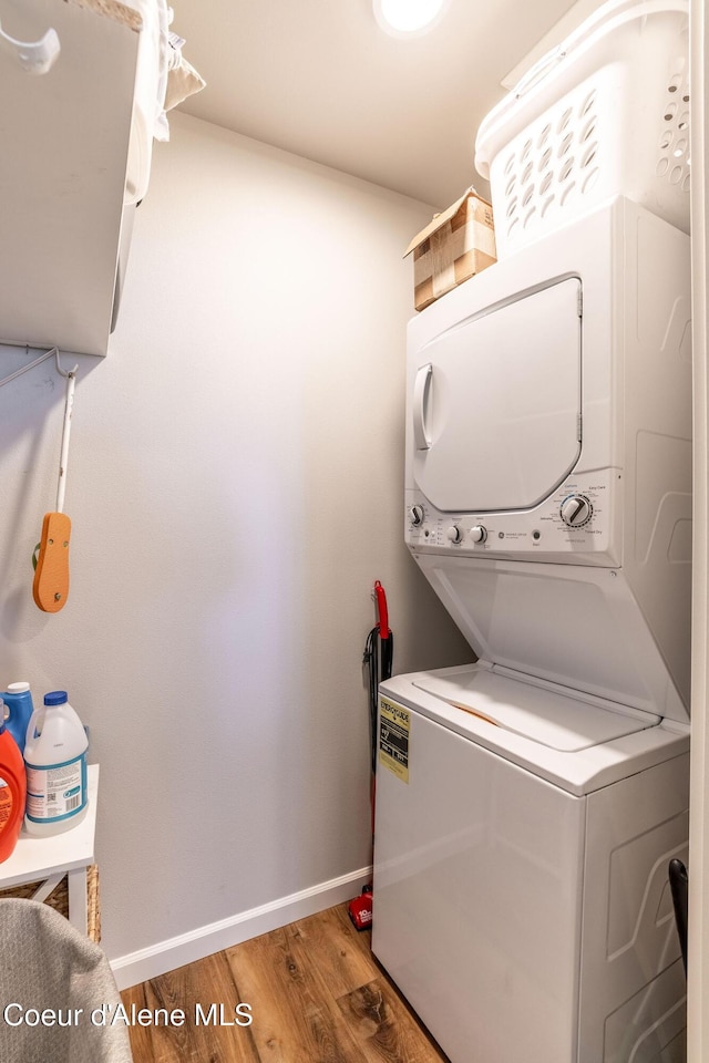 clothes washing area featuring laundry area, light wood finished floors, stacked washer / dryer, and baseboards