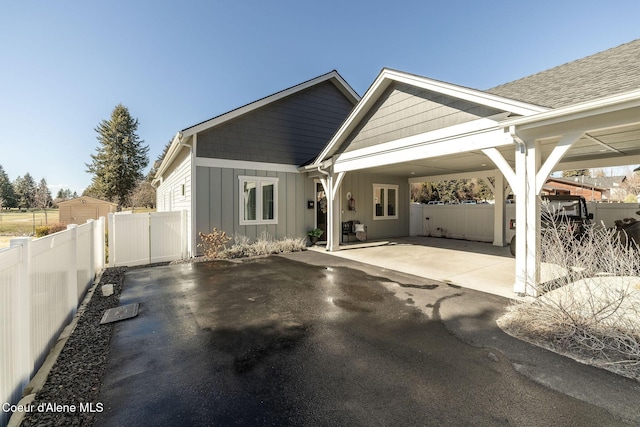 view of front of house with driveway, board and batten siding, a patio, fence, and a carport