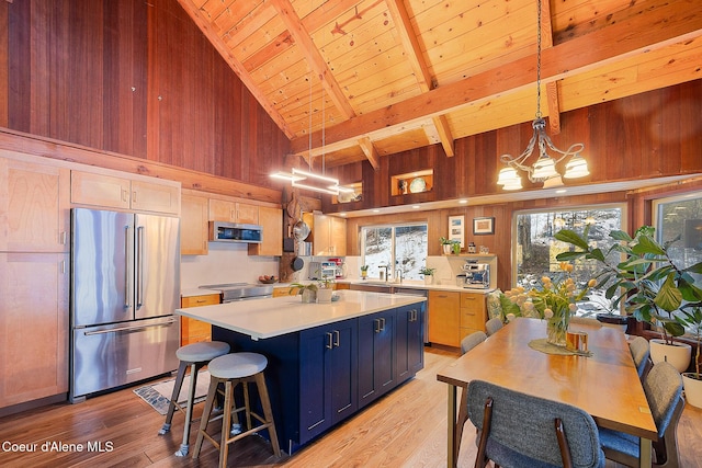 kitchen featuring hanging light fixtures, a kitchen island, light brown cabinets, appliances with stainless steel finishes, and wooden walls