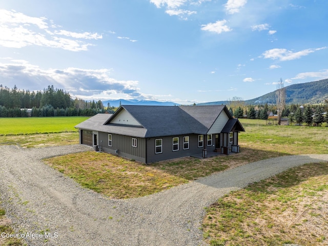 view of front facade featuring an attached garage, a front lawn, gravel driveway, and a mountain view