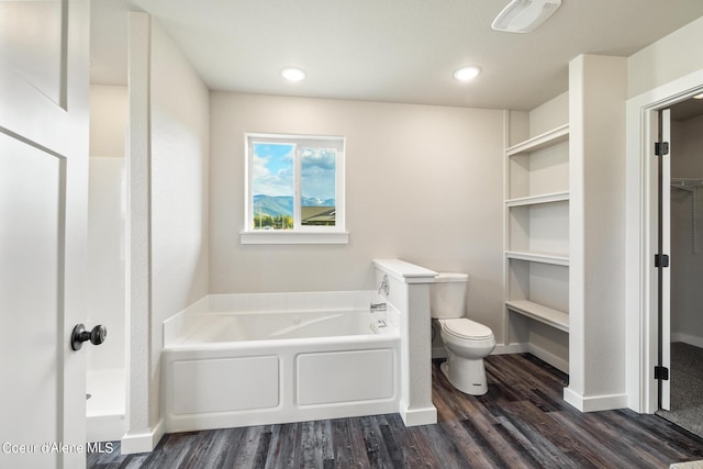 bathroom featuring a walk in closet, toilet, wood finished floors, baseboards, and a bath