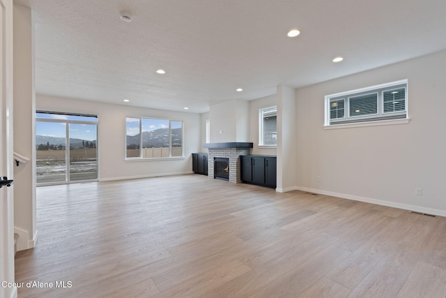 unfurnished living room featuring beverage cooler, a brick fireplace, light hardwood / wood-style flooring, and a textured ceiling