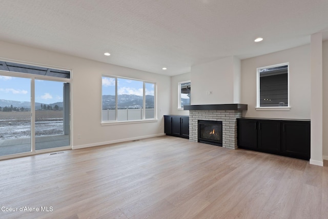 unfurnished living room with a fireplace, a mountain view, a textured ceiling, and light wood-type flooring