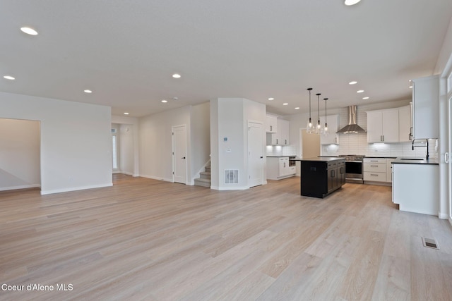 kitchen featuring wall chimney range hood, backsplash, a center island, white cabinets, and decorative light fixtures