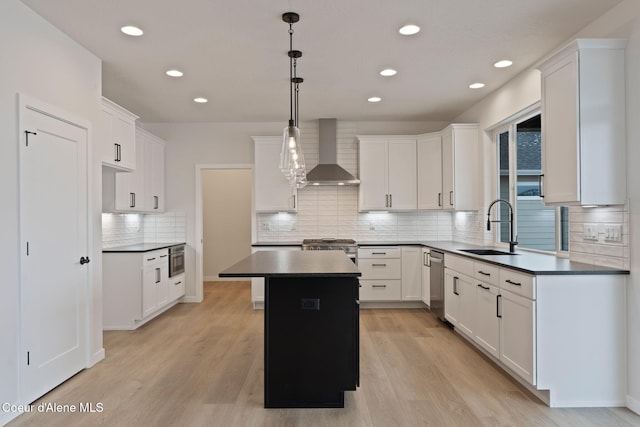 kitchen featuring pendant lighting, sink, white cabinets, a center island, and wall chimney range hood