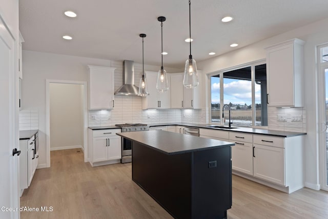 kitchen featuring pendant lighting, wall chimney range hood, sink, stainless steel appliances, and white cabinets