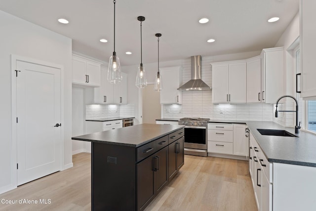 kitchen featuring wall chimney exhaust hood, sink, stainless steel stove, a kitchen island, and white cabinets