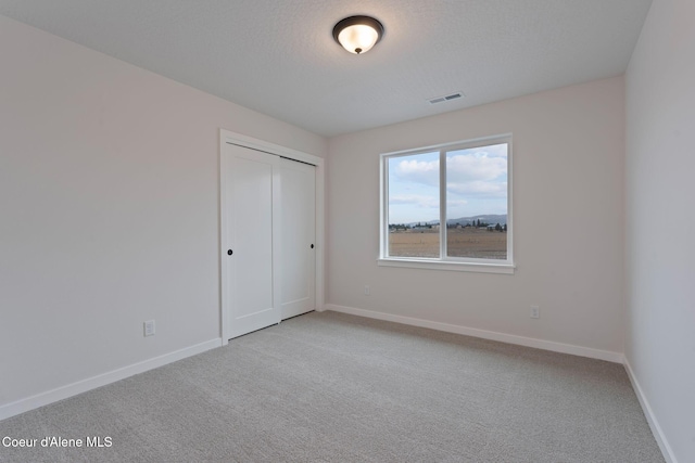 unfurnished bedroom with light colored carpet, a textured ceiling, and a closet