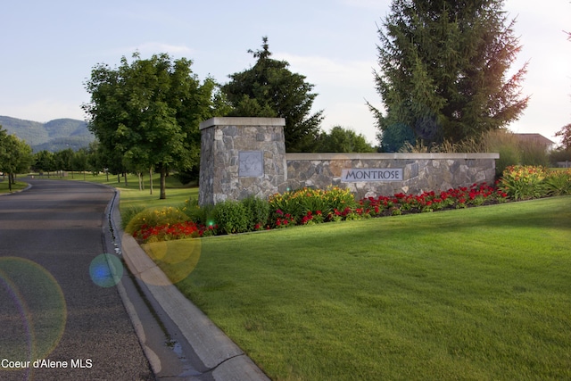 community / neighborhood sign featuring a mountain view and a lawn