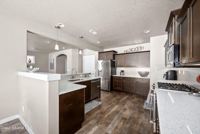 kitchen with appliances with stainless steel finishes, sink, hanging light fixtures, light stone countertops, and dark wood-type flooring