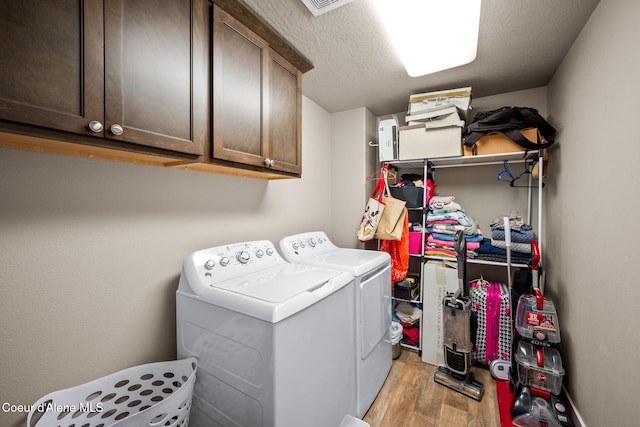 clothes washing area featuring light hardwood / wood-style flooring, washing machine and dryer, cabinets, and a textured ceiling